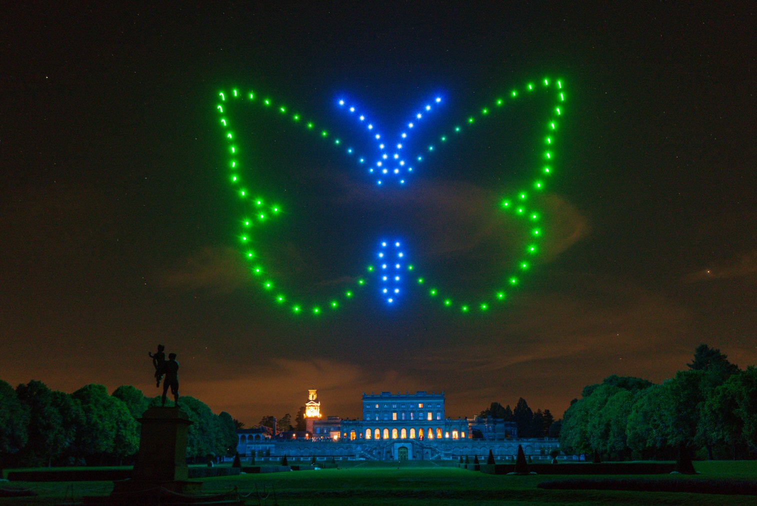 A green and blue butterfly drone formation above Cliveden at night