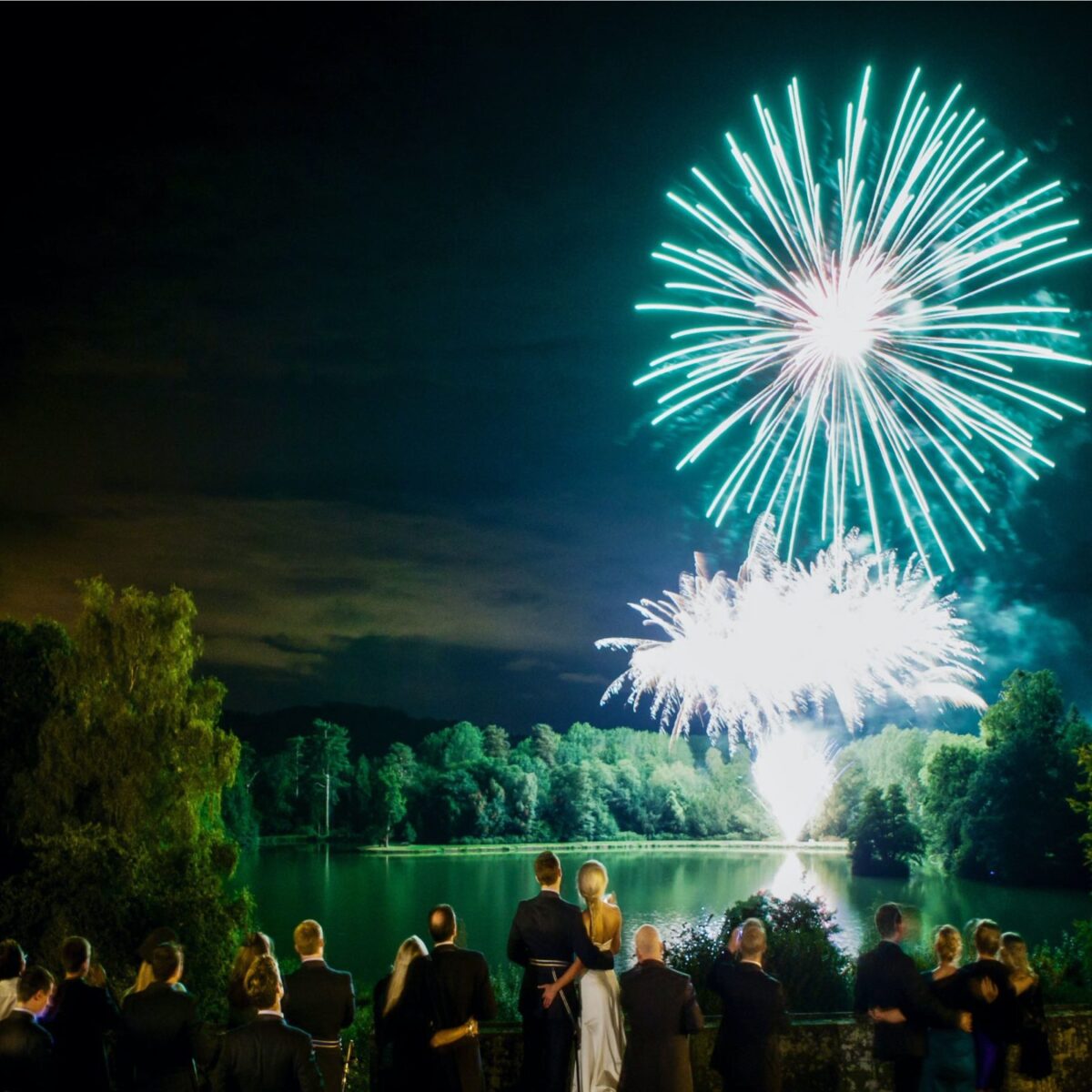 A colourful MLE fireworks display above a lake with guests watching