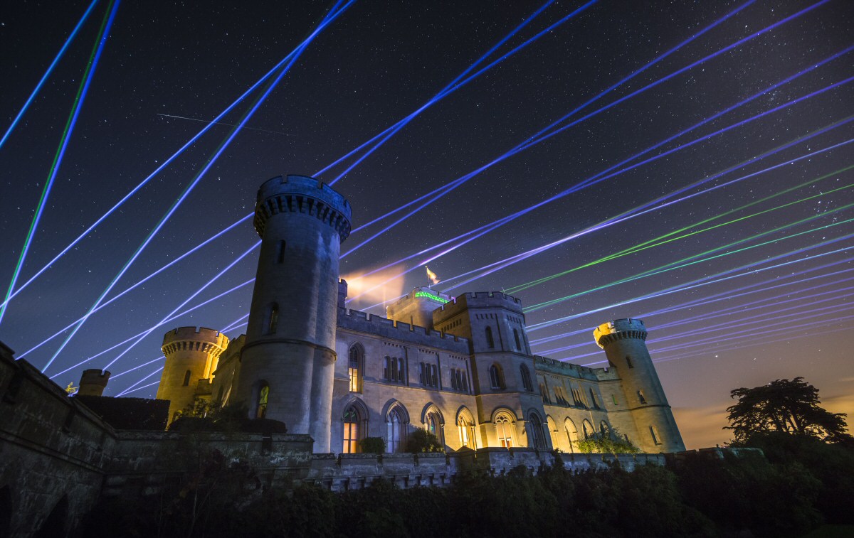 Blue and green laser beams illuminating the sky above Eastnor Castle